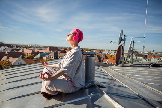 Woman with headphones meditating on rooftop