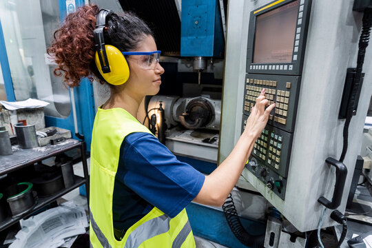 Engineer in protective workwear operating CNC machine in modern factory