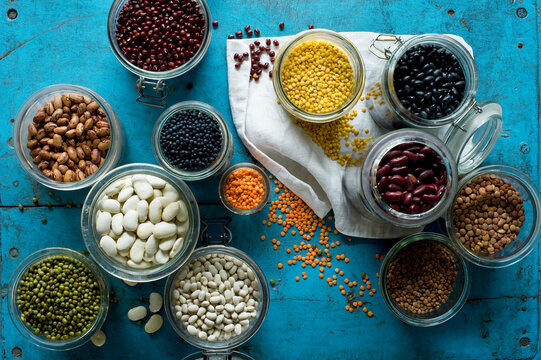 Various beans and lentils in jars on blue rustic wooden surface