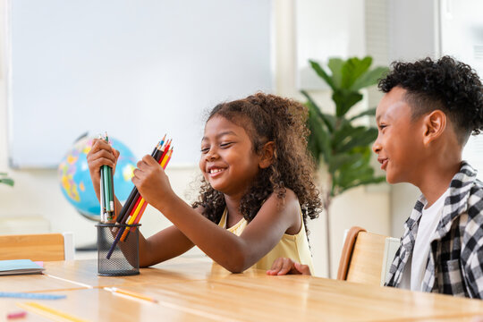 Diverse students playing with colorful pencils in classroom environment, Happy school children enjoying creative learning activity at school desk, Primary students sharing school supplies in classroom