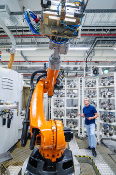 Engineer standing by industrial robot arm in automated factory