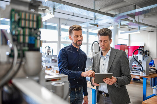 Employees discussing technology on tablet in production hall