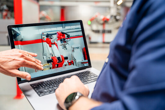 Employees pointing at laptop screen showing industrial robot