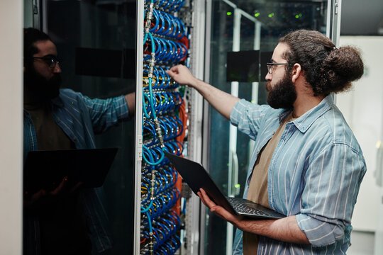 Technician connecting cable on server holding laptop in server room
