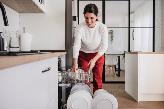 Smiling woman arranging cups in dishwasher at home