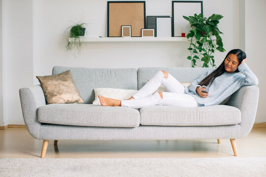 Young woman relaxing on couch in the living room using smartphone