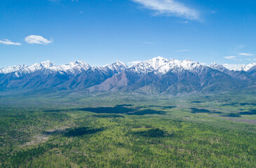 Fototapeta premium Panoramic view of majestic snow-capped mountains stand tall over a vast green plain on a sunny day