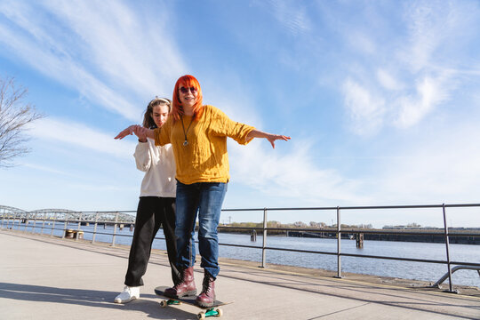 Son helping mother balance on a skateboard by the river