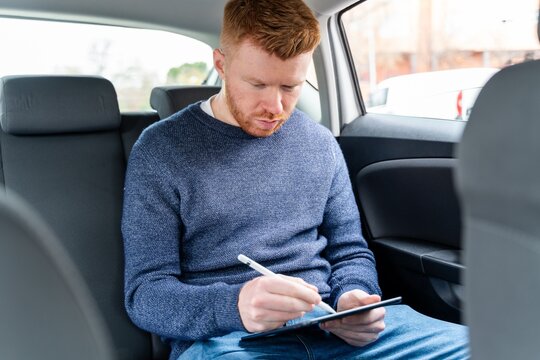 Businessman working on a digital tablet in the back seat of a car