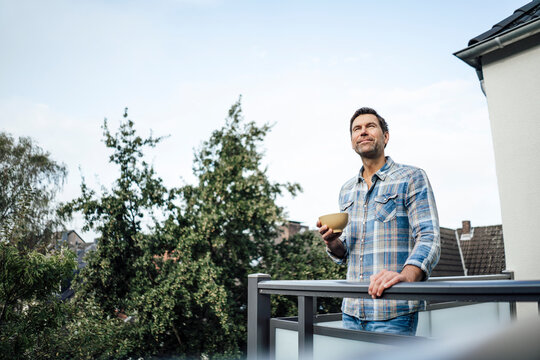 Mature man day dreaming while holding bowl in balcony of house