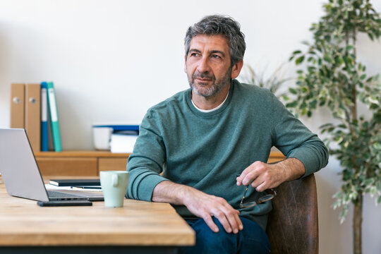 Confident businessman sitting at desk thinking indoors