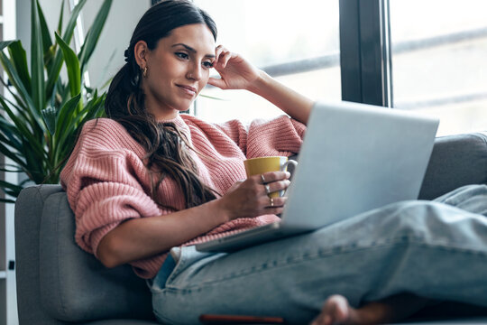 Student relaxing on cozy sofa with laptop doing homework