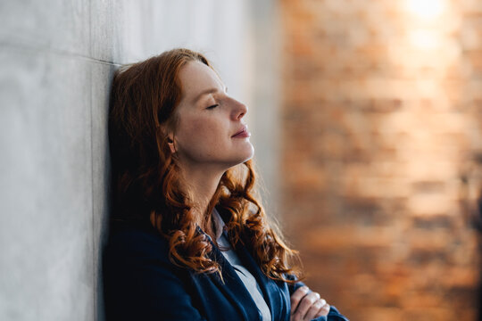 Redheaded businesswoman having a break leaning against a wall in office
