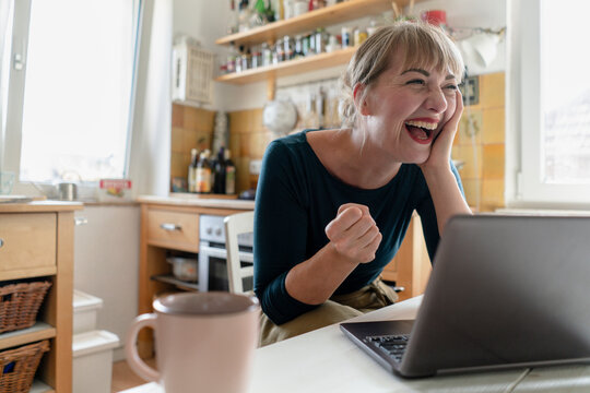 Portrait of woman sitting in the kitchen with laptop crying for joy