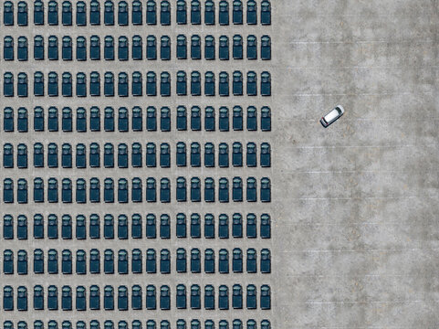 Aerial view of white car leaving parking lot filled with black cars
