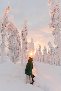 Young woman with snowboard standing on snow-covered field during sunrise