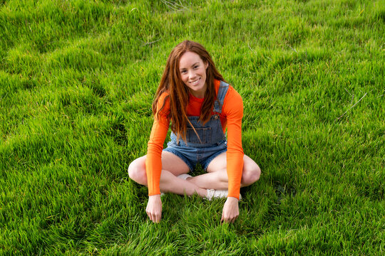 Smiling redhead sitting on green grass in a field in Spain