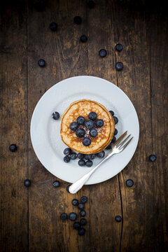 Dish with pile of pancakes, blueberries, sprinkled with icing sugar