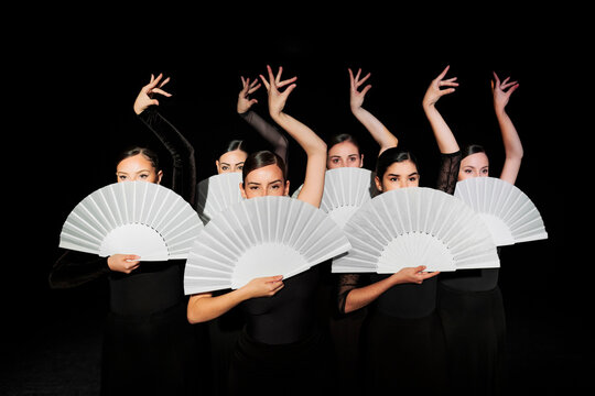 Group of flamenco dancers holding hand fans and dancing against black background