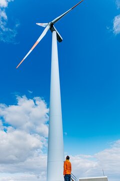 Man in jacket looking up at tall wind turbine outdoors
