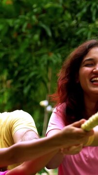 Indian family playing tug of war rassi khech in home garden, spending quality fun time together enjoying outdoor sports, cheerful Asian parents children bonding through traditional backyard activity