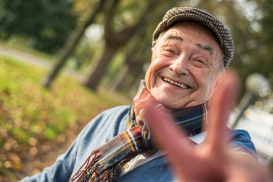 Portrait of happy senior man outdoors doing victory sign