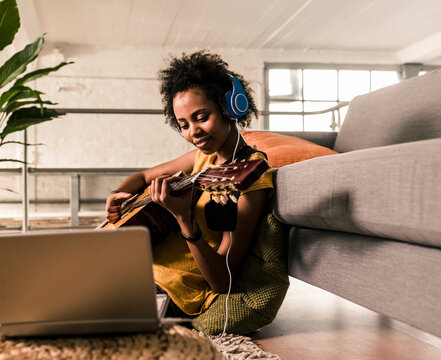 Young woman at home with headphones and laptop playing guitar