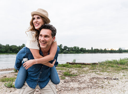 Happy man carrying girlfriend piggyback at the riverside