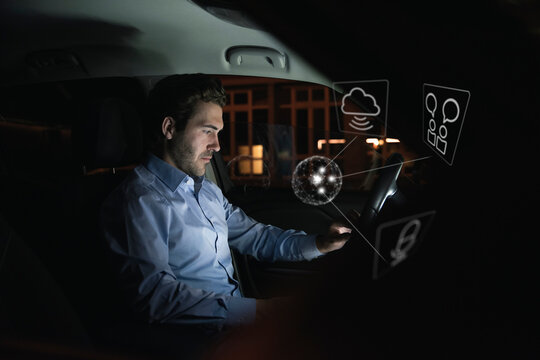 Businessman using device in car at night surrounded by internet symbols