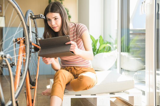 Young woman with tablet reparing bicycle at home