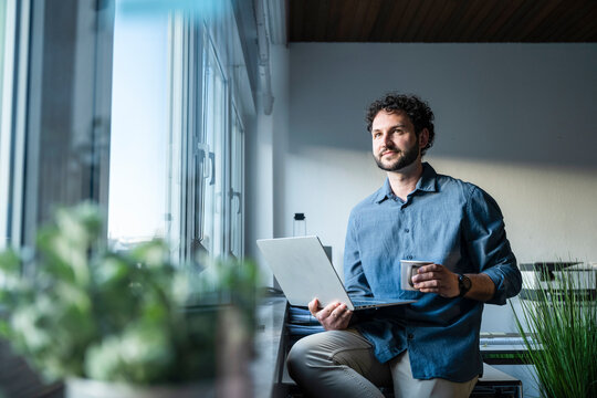Businessman brainstorming with notebook and coffee by office window