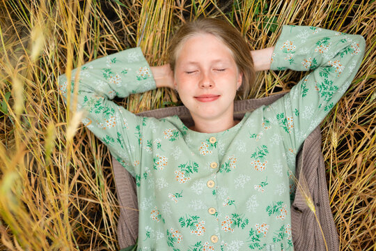 Young woman relaxing happily in a summer wheat field wearing a vintage dress