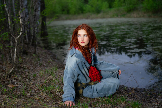 Model with red hair sitting by a forest swamp in summer