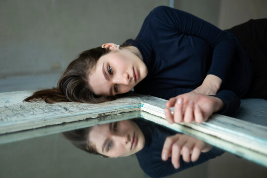 Model lying on floor looking at mirror reflection in sadness