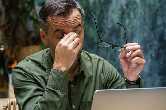 Tired businessman with head in hands working on laptop while sitting at cafe