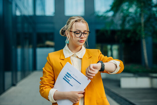 Businesswoman checking watch holding document outdoor