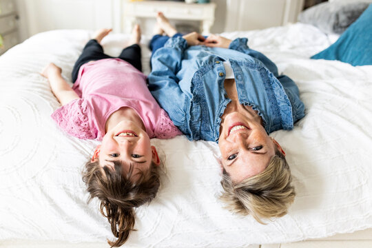 Happy mother and daughter lying on bed at home