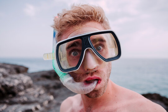 Portrait of young man with diving goggles and snorkel pulling funny faces