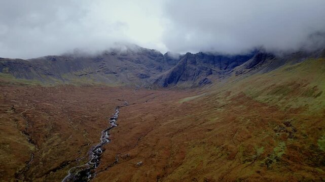 Aerial drone flyover up Coire na creiche toward Sgurr an Fheadain and Waterpipe Gully near the Fairy Pools, Isle of Skye. Moody, overcast Scottish Highlands with low grey cloud and dramatic peaks.