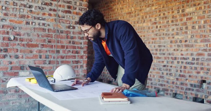 Writing, reading and man with blueprint at construction site, planning update or change for renovation. Engineering, remodeling or architect with revision of schematic, laptop or property development