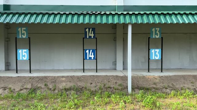 Numbered outdoor shooting lanes under a green metal roof, a sports training complex with target markers