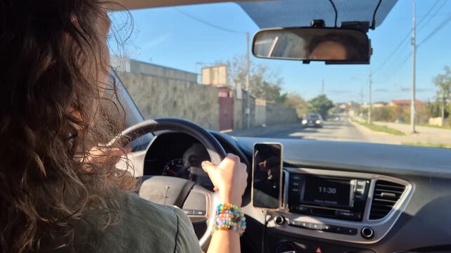 Driving car woman, view from passenger seat traveling on a sunny suburban street during daily commute.