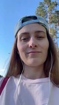 A young woman wearing a backwards baseball cap and headphones listens to music in a sunny pine forest