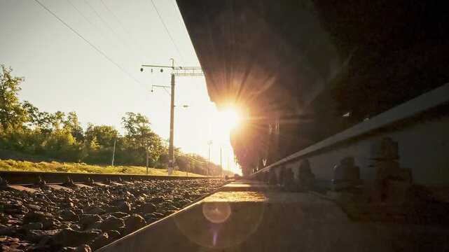 In the rolling countryside, a freight train rushes along iron rails, a close-up capturing its rotating wheelsets. The view emphasizes streamlined logistics and sustainable infrastructure progress
