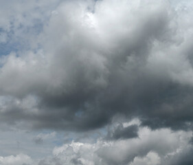 Obraz premium Horizontal close up of a mostly cloudy sky with a large dark storm cloud dominating the frame, scattered white clouds, and small blue patches showing through