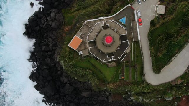 Majestic aerial top down view of the Ponta do Arnel lighthouse on Sao Miguel Island, Azores, as ocean waves crash on the volcanic shore