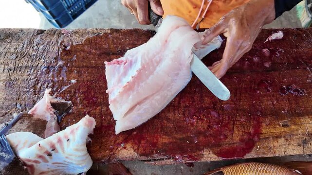 Zenith overview of man hands filleting fresh fish on market table with flies buzzing around, cleaning skin off expertly