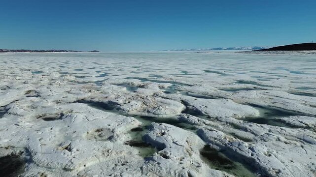 Low aerial drone shot over ice floes covered in brilliant turquoise meltwater pools during the seasonal Arctic break-up.