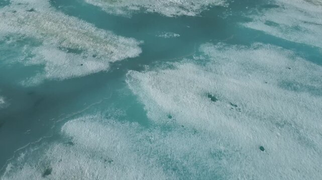 Top-down aerial abstract shot of turquoise water channels cutting through deteriorating white sea ice patterns.