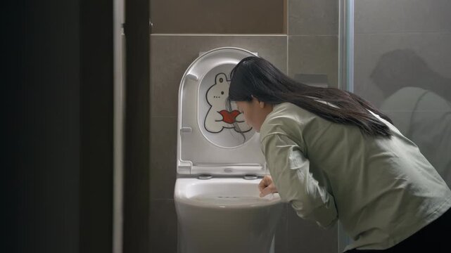 Tired young woman feeling sick and vomit into toilet bowl sitting on bathroom floor due to early stages of pregnancy or food poisoning or drinking alcohol intoxication, drunkenness, nausea, illness